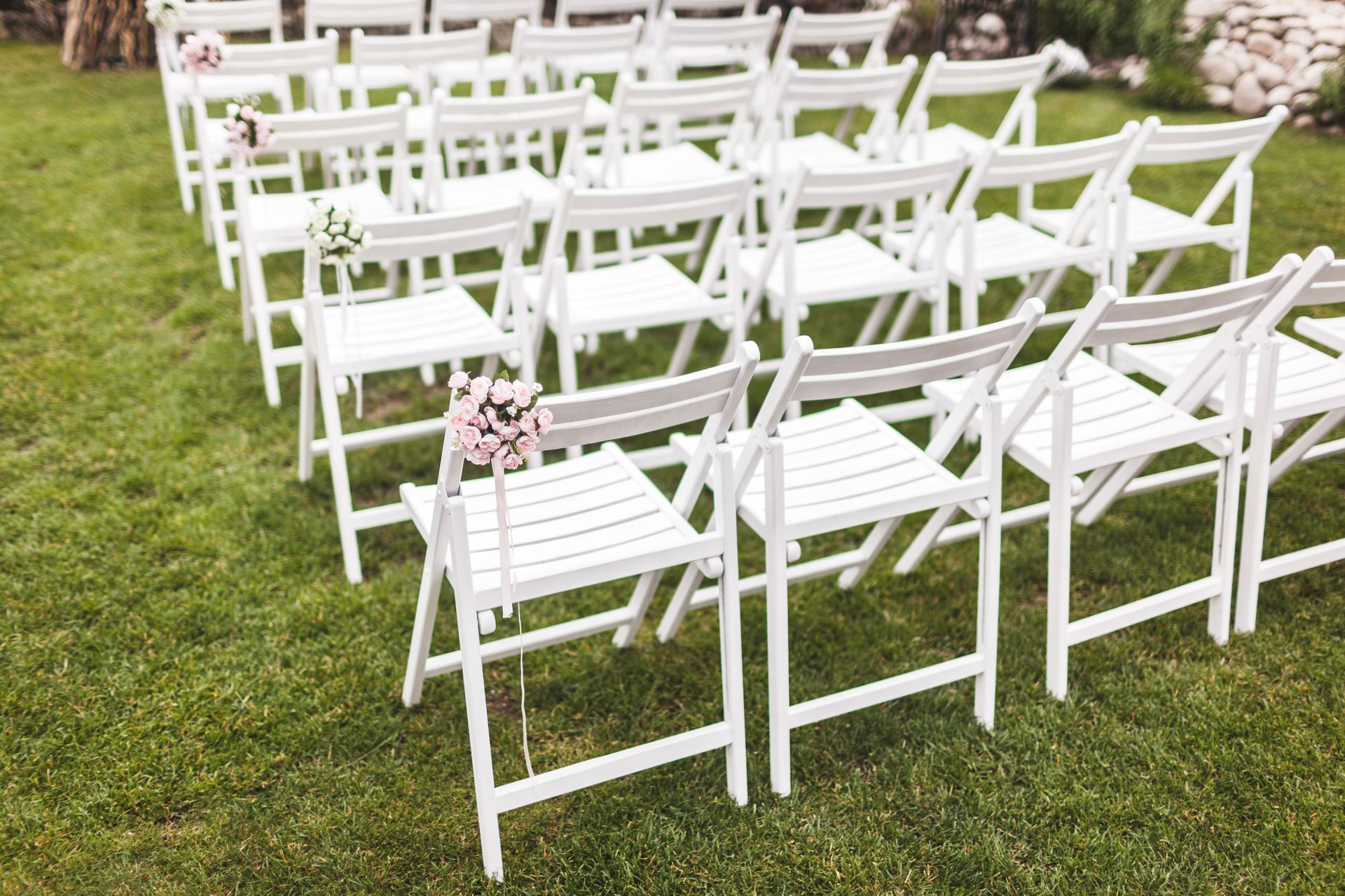 A row of white folding chairs sitting on top of a lush green field.