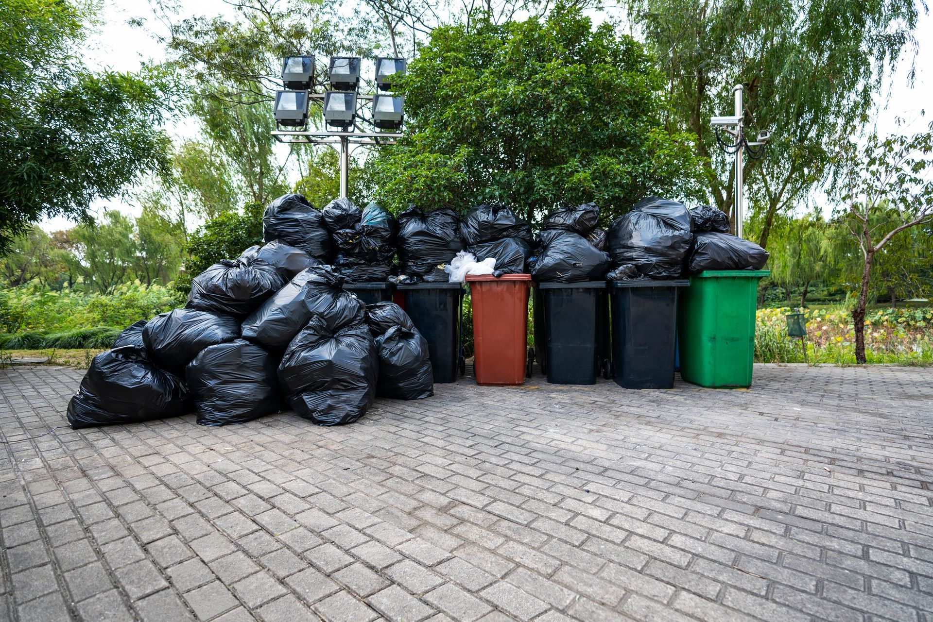 A pile of garbage bags and trash cans on a brick sidewalk.
