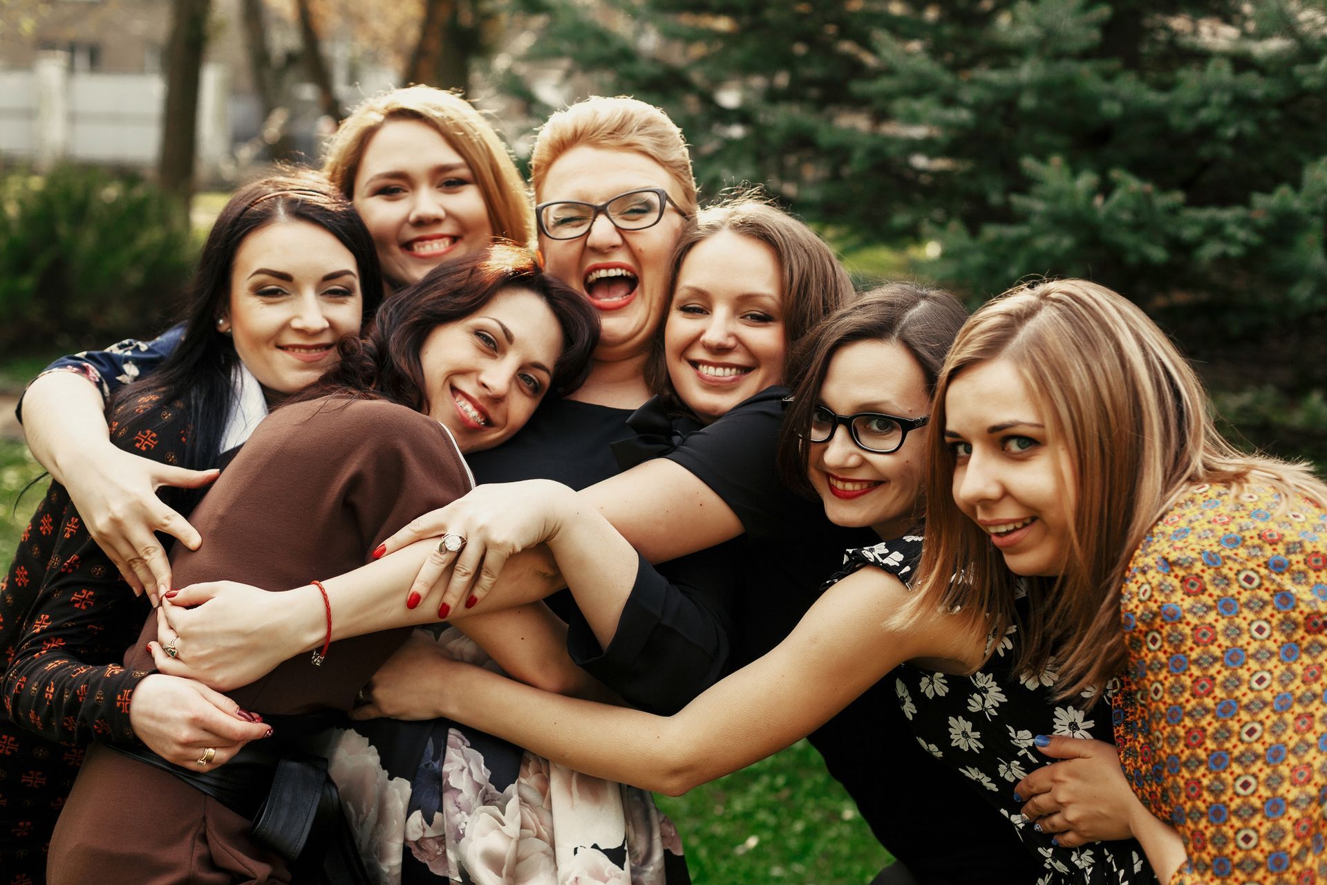 A group of women are hugging each other in a park.