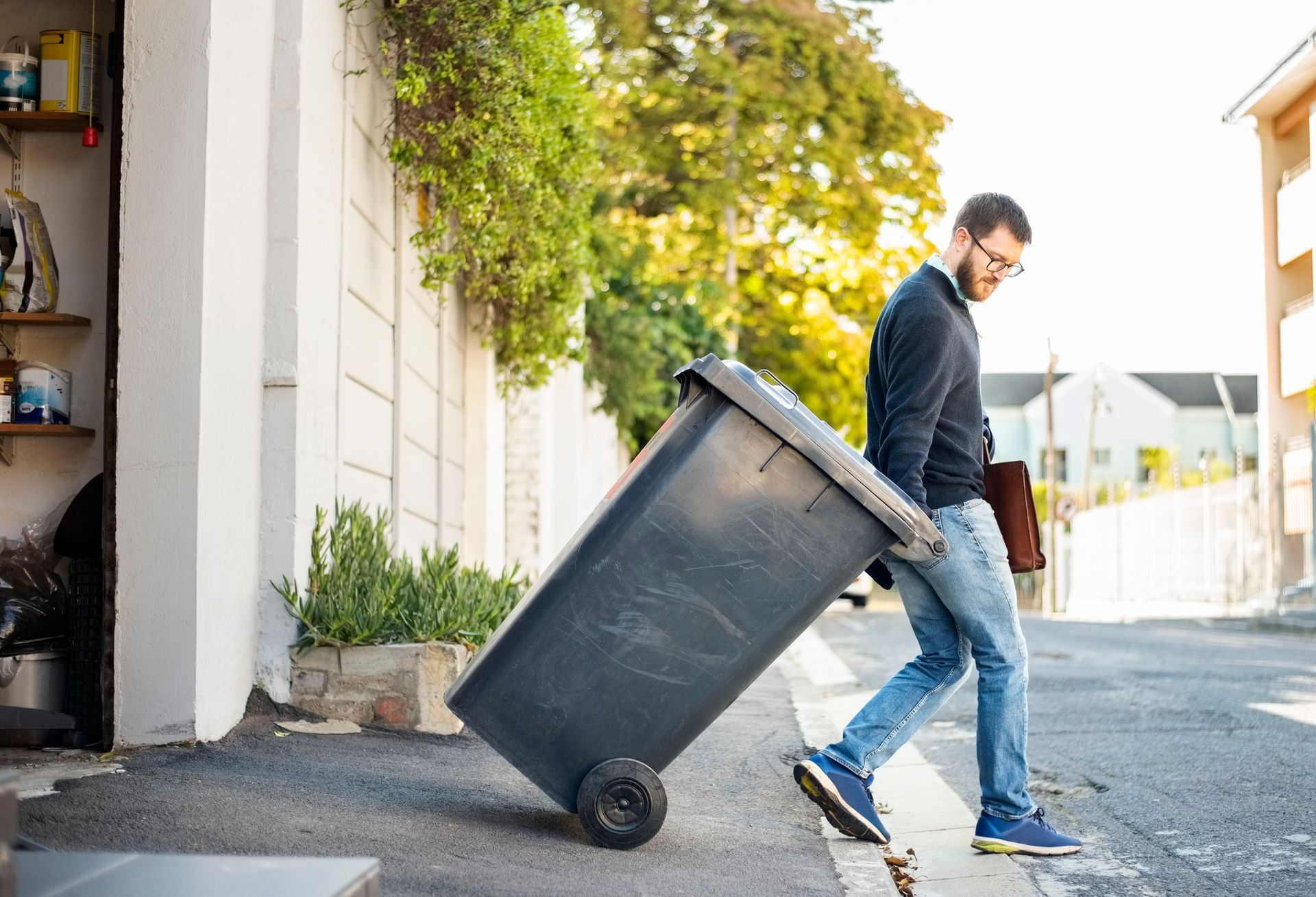 A man is pushing a trash can down a sidewalk.