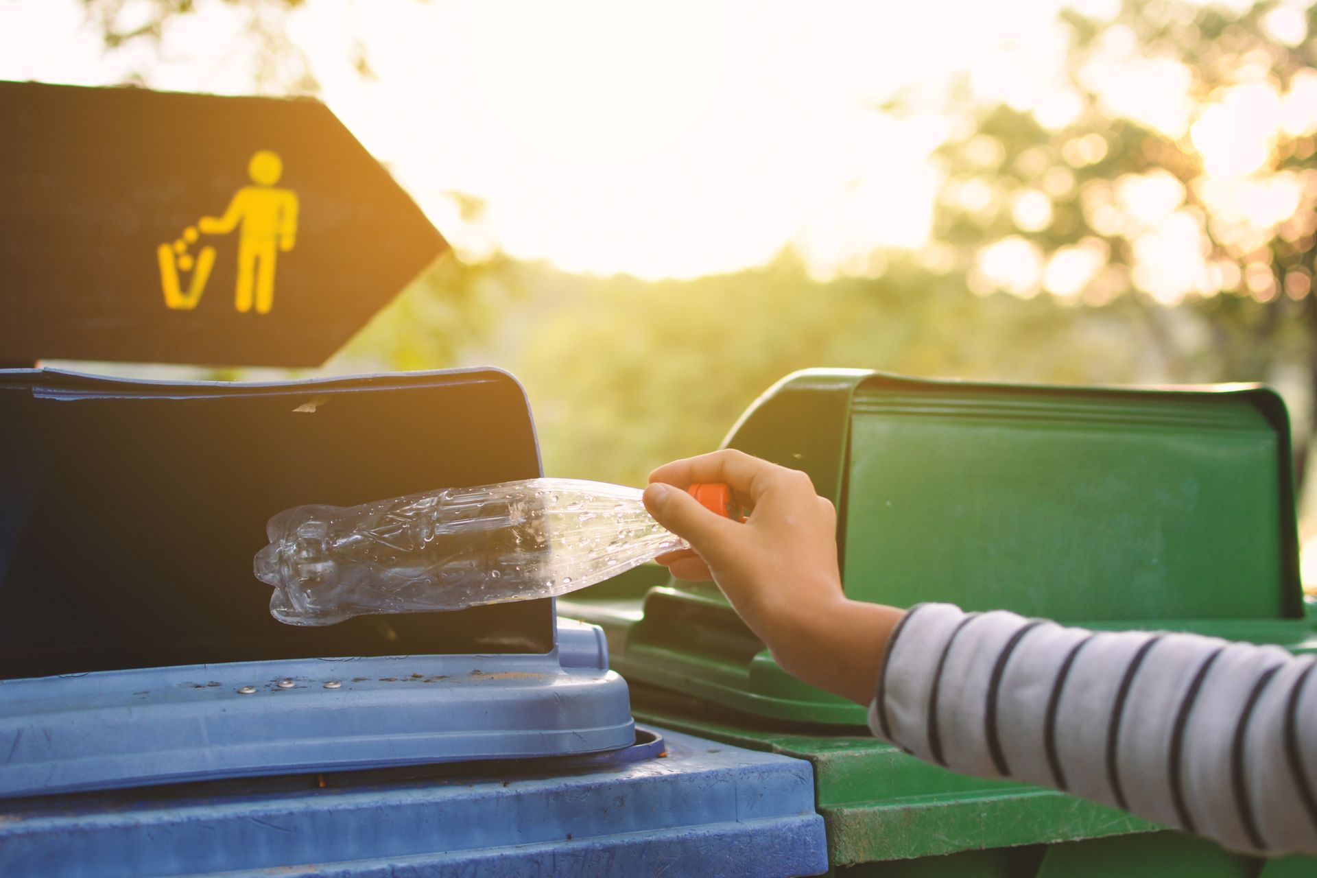 A person is throwing a plastic bottle into a trash can.