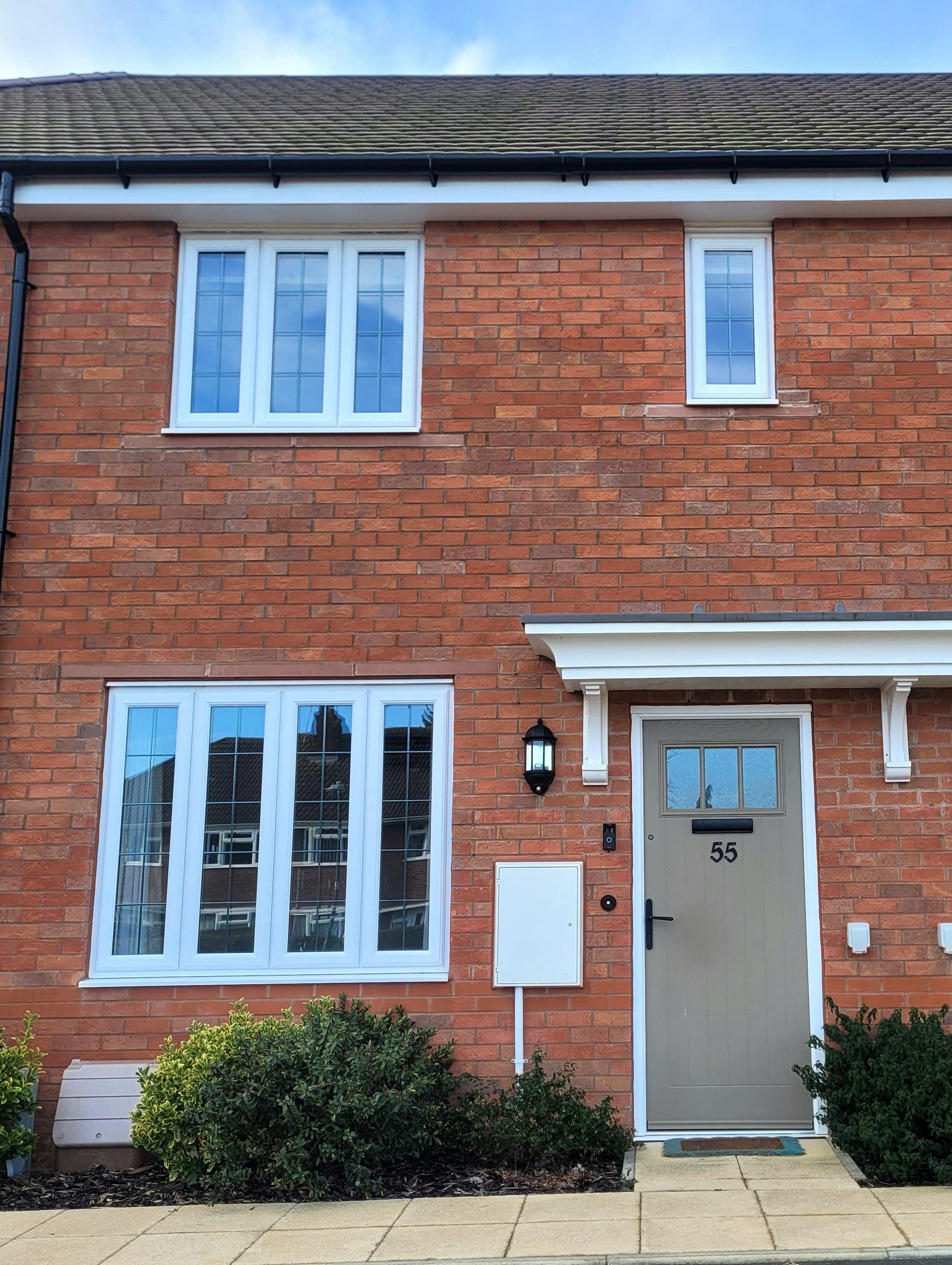 Red brick townhouse with white trim, a tan door, and blue sky.
