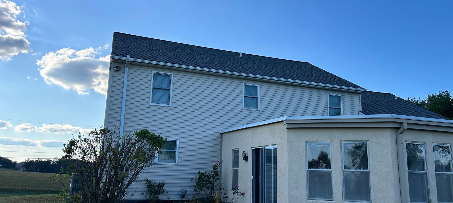 A two-story house with a dark gray roof against a blue sky with clouds.