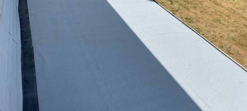 A gray rooftop with a dark strip on the left side, grass on the right, and a shadow across the center.