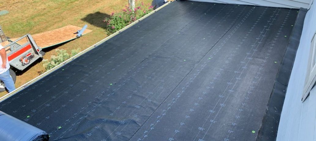 A flat roof covered in black material, adjacent to a white building.
