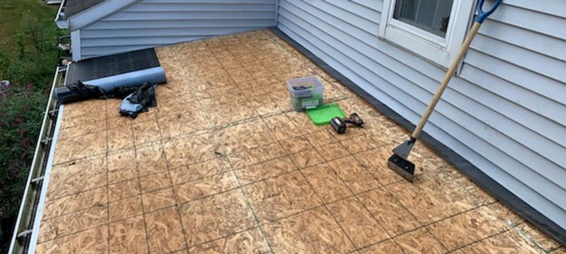 Rooftop with tools and materials for repair, next to a gray house.