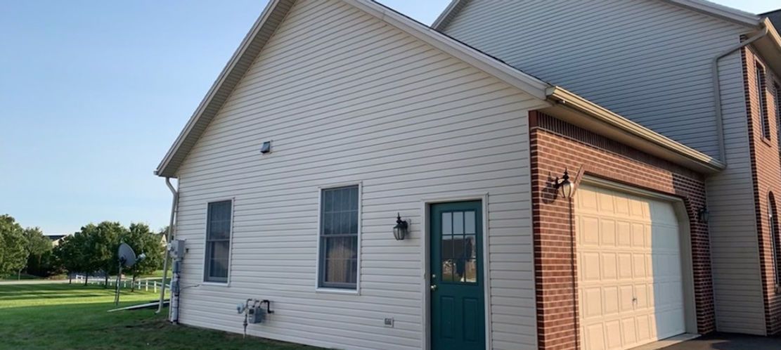 Exterior of a light-colored house with a brick garage, a green door, and blue sky.