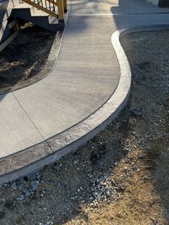 A curved concrete walkway bordered by decorative stone blocks, leading to a set of wooden outdoor stairs.