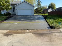 A newly poured concrete driveway leads to a suburban garage, blocked off by yellow caution tape.