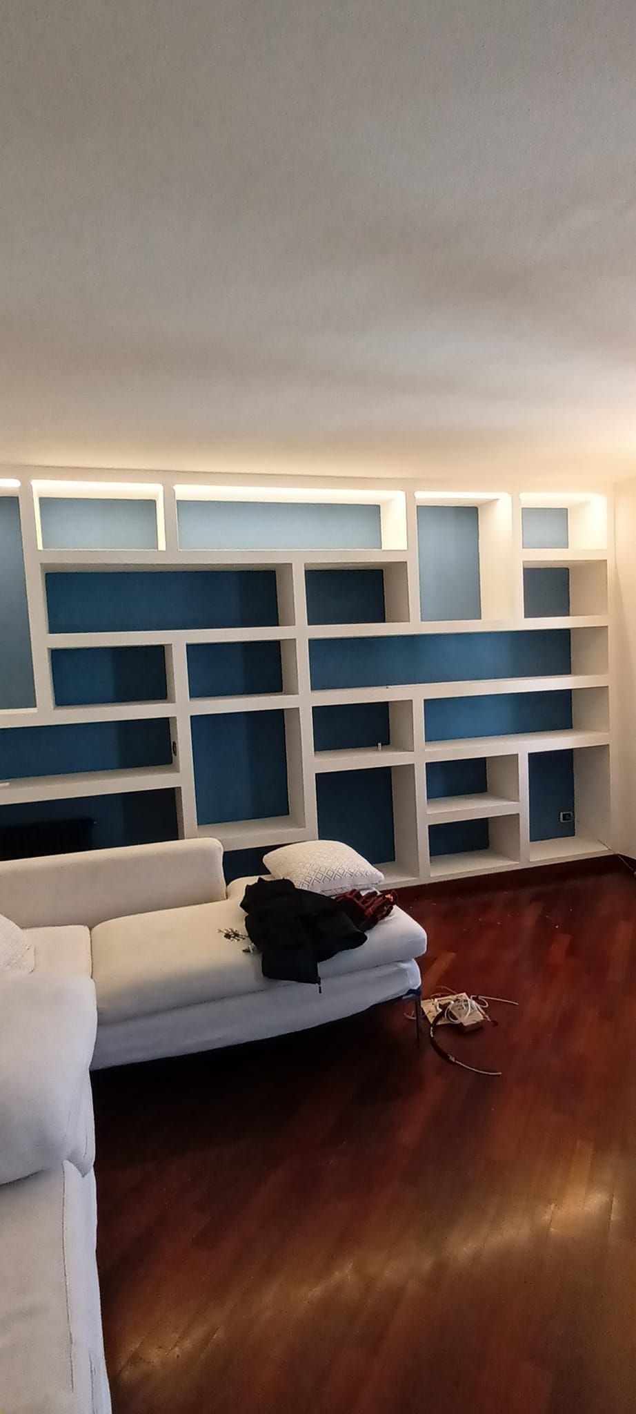 Un soggiorno con una libreria bianca incorporata, un divano bianco e pavimenti in legno scuro.