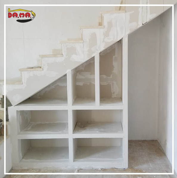 Scala in costruzione con ripiani portaoggetti integrati. Pareti bianche, scale grezze.