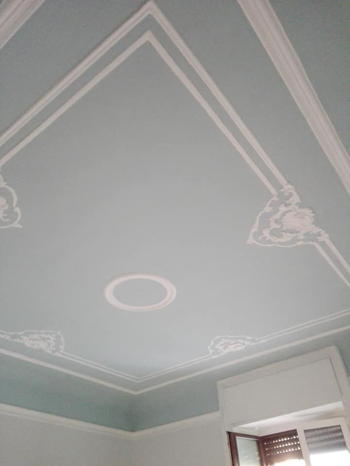 Soffitto azzurro con modanature decorative bianche e dettaglio circolare centrale.