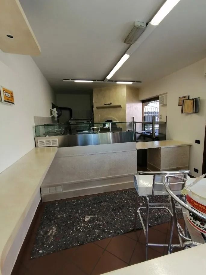 Interno di un ristorante vuoto con banconi in acciaio inossidabile, illuminazione dall'alto e pavimento scuro.