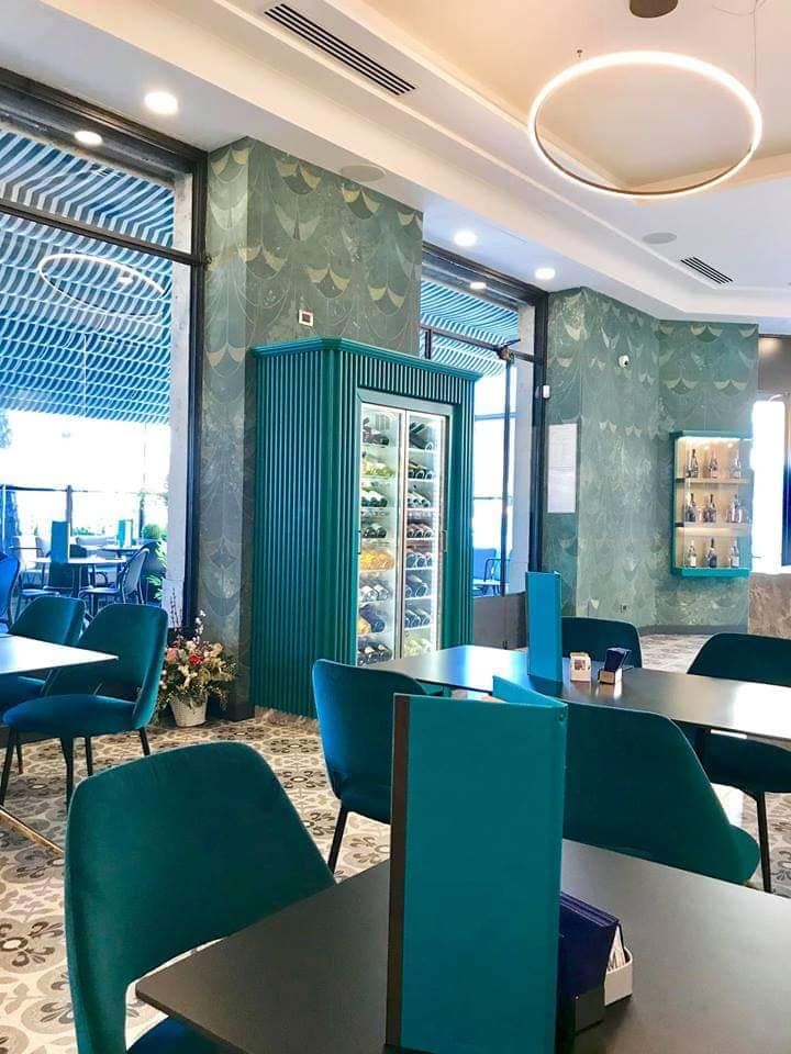 L'interno di un ristorante con dettagli color verde acqua: sedie, decorazioni murali e un refrigeratore per il vino.