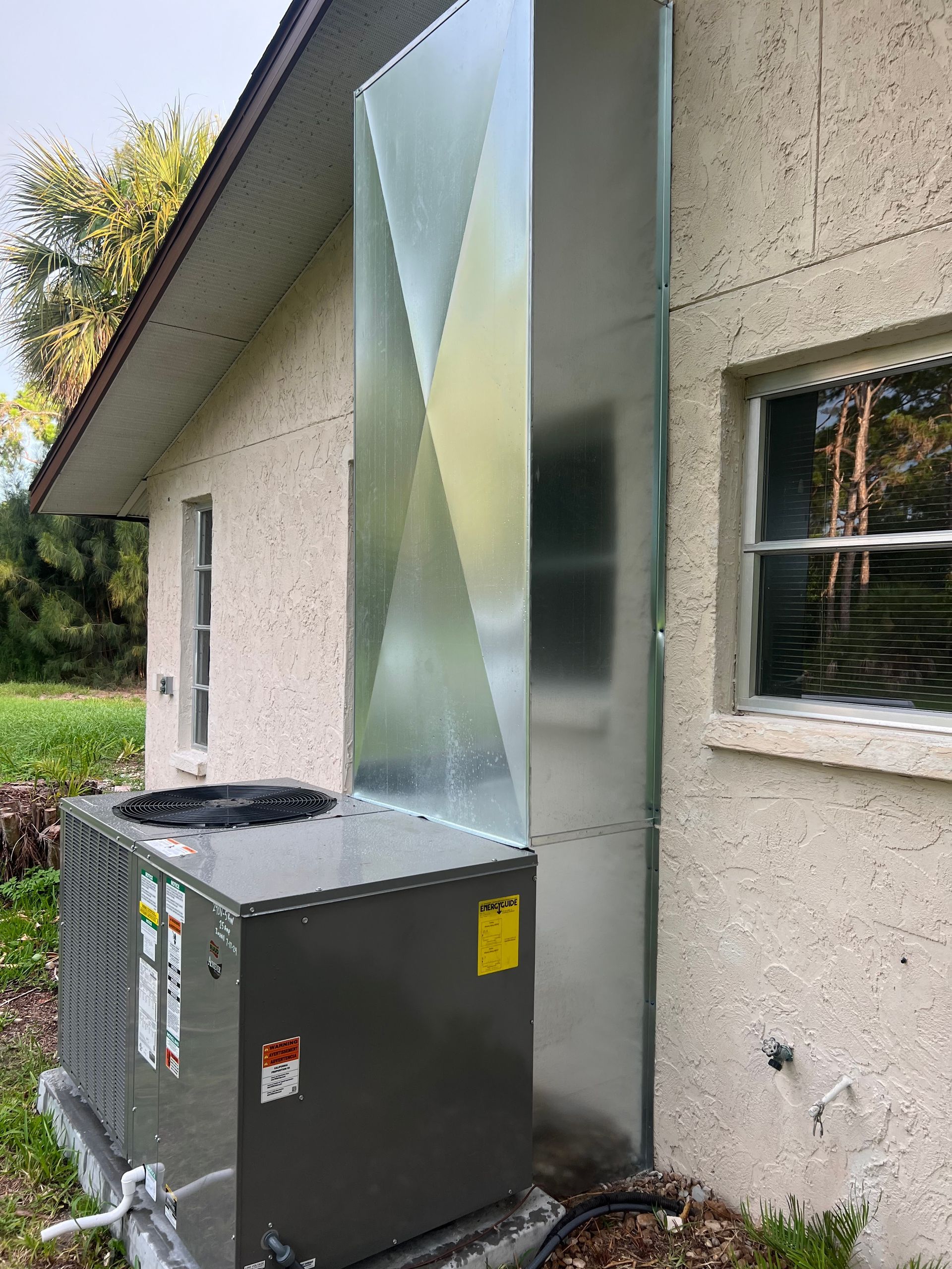 HVAC unit outside a building with a large metal duct against the wall.