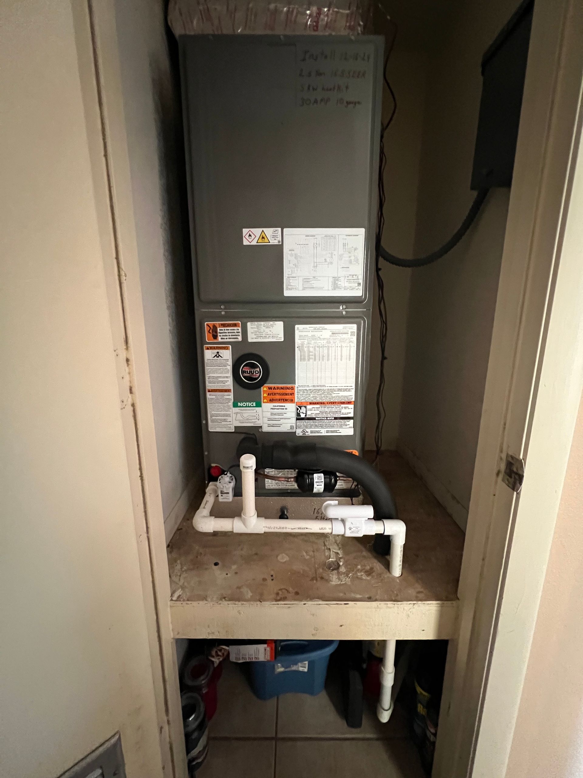 Air conditioning unit in a closet with PVC piping, electrical box, and ductwork.