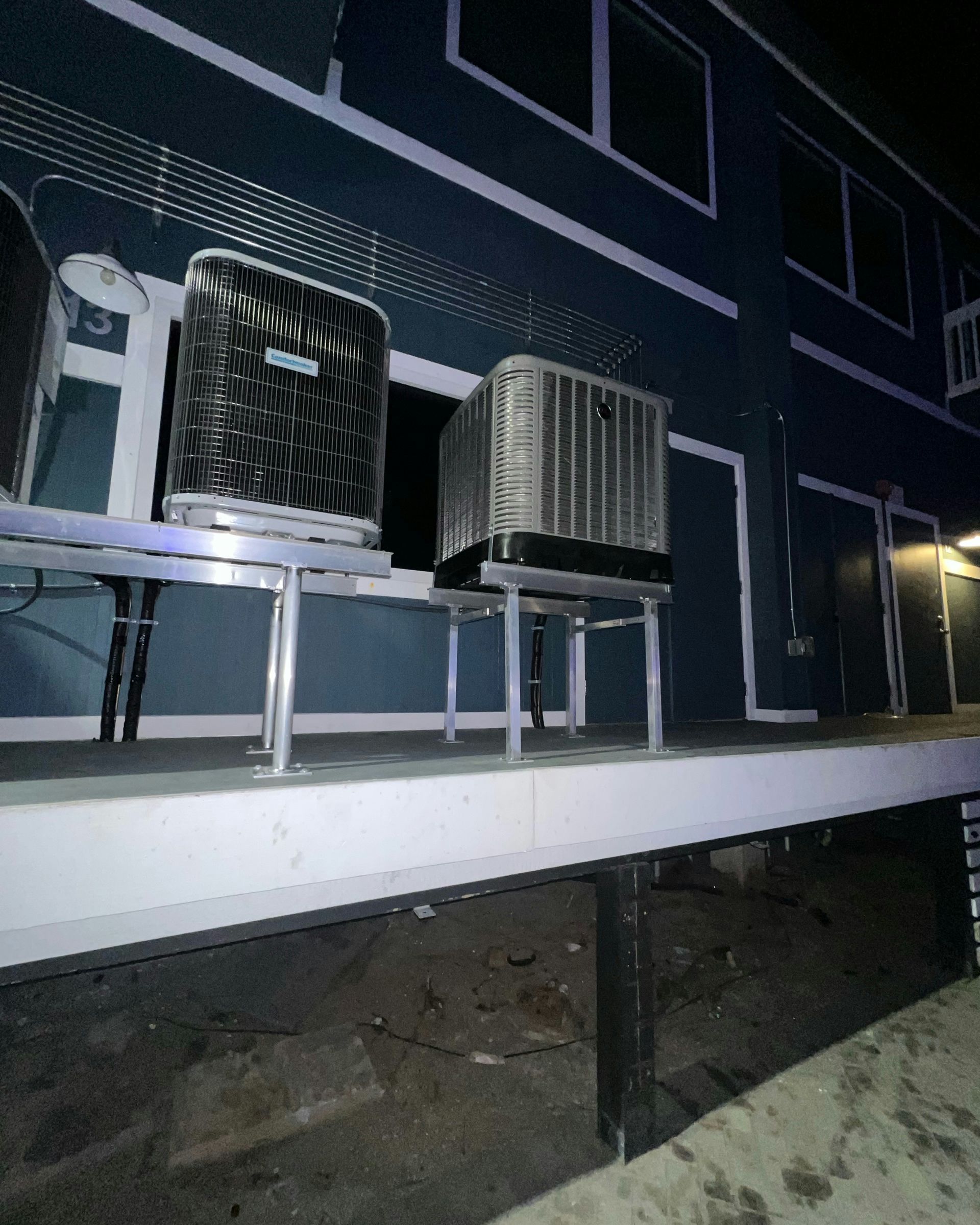 Air conditioning units on a metal platform attached to a blue building at night.
