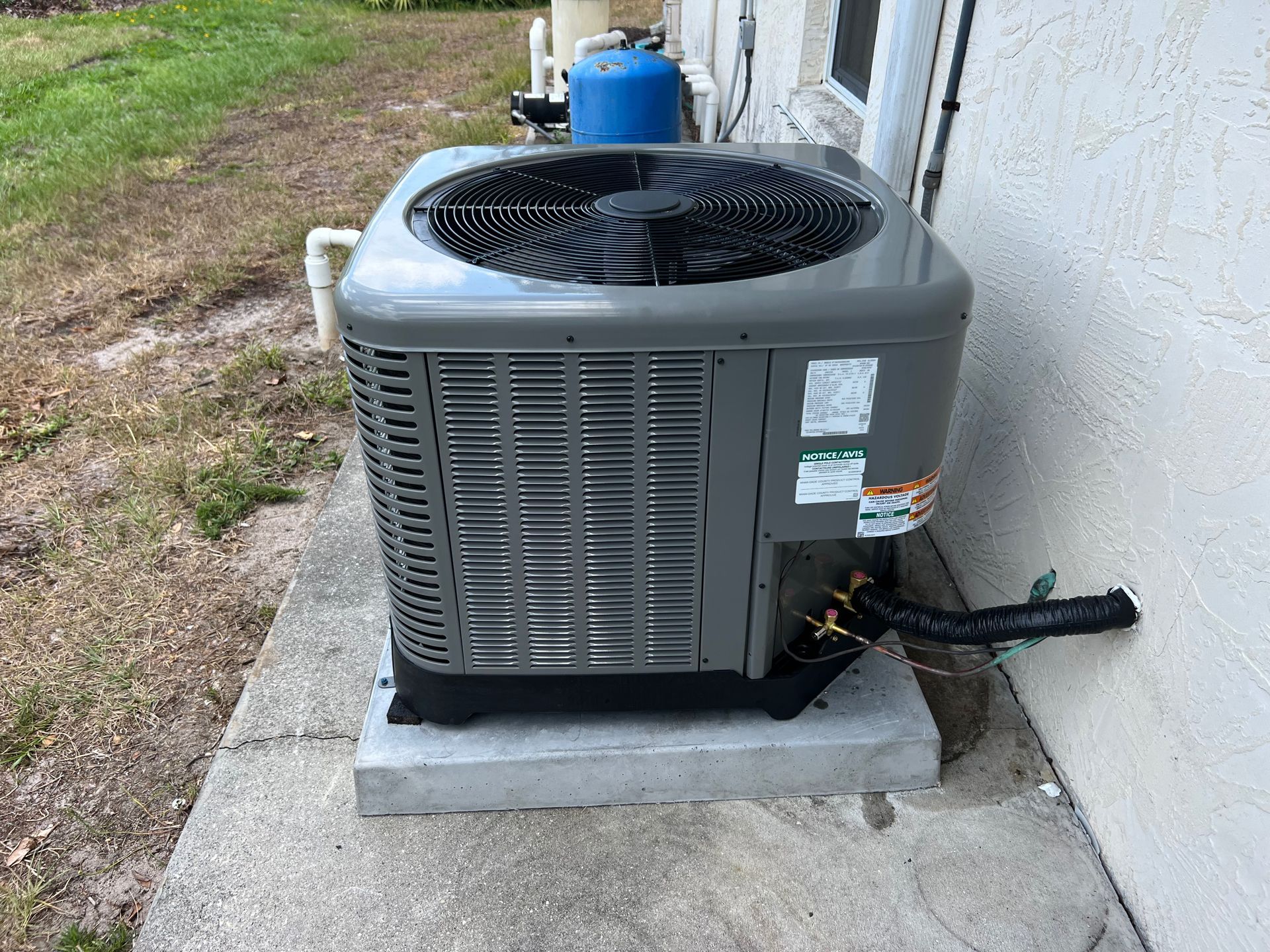Gray air conditioning unit on a concrete base next to a white wall.