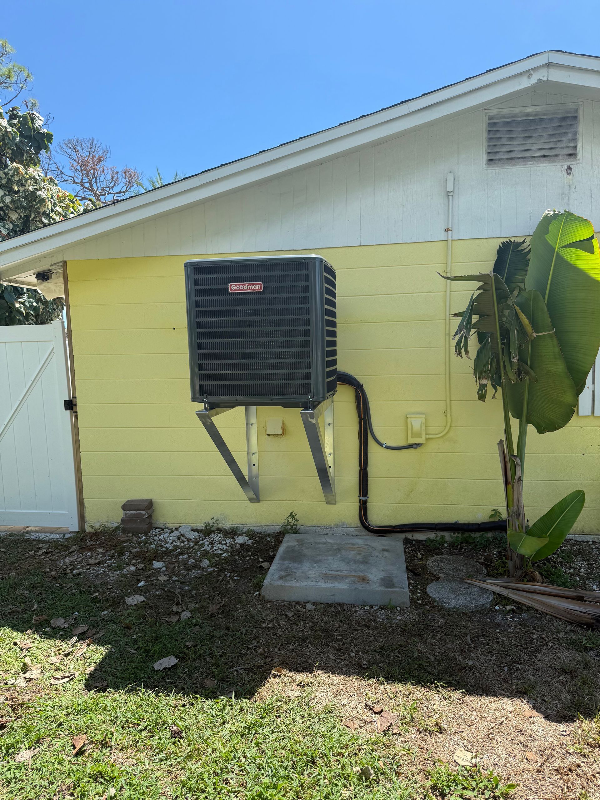 An air conditioning unit mounted on a yellow exterior wall, next to a plant.