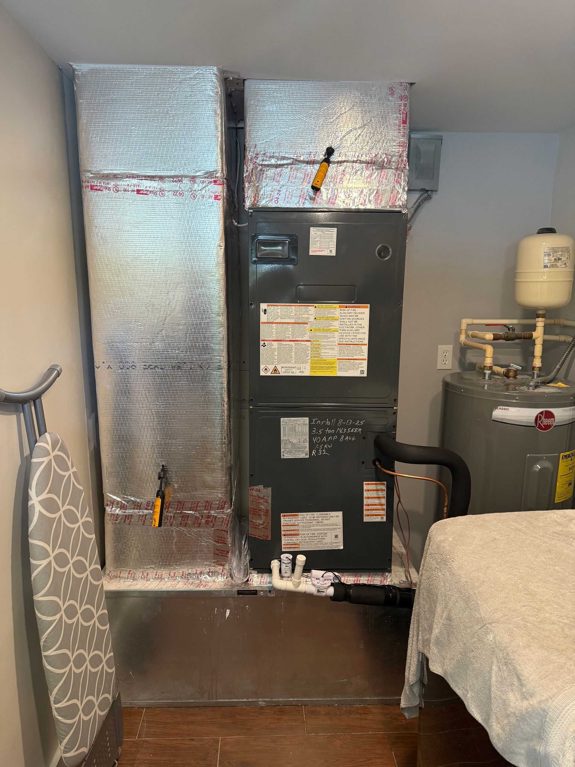 HVAC unit with insulated ductwork, installed near a water heater and covered object in a room.