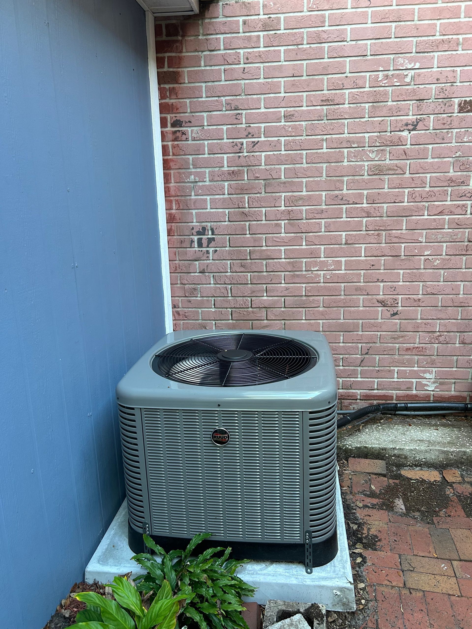 Air conditioning unit against a brick wall and a blue wall.
