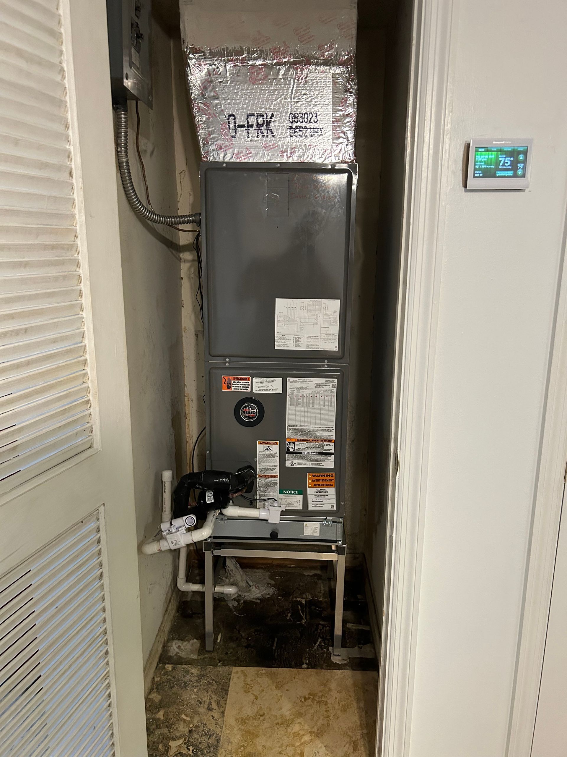 HVAC unit in a narrow utility closet, with ductwork and a thermostat on the wall.