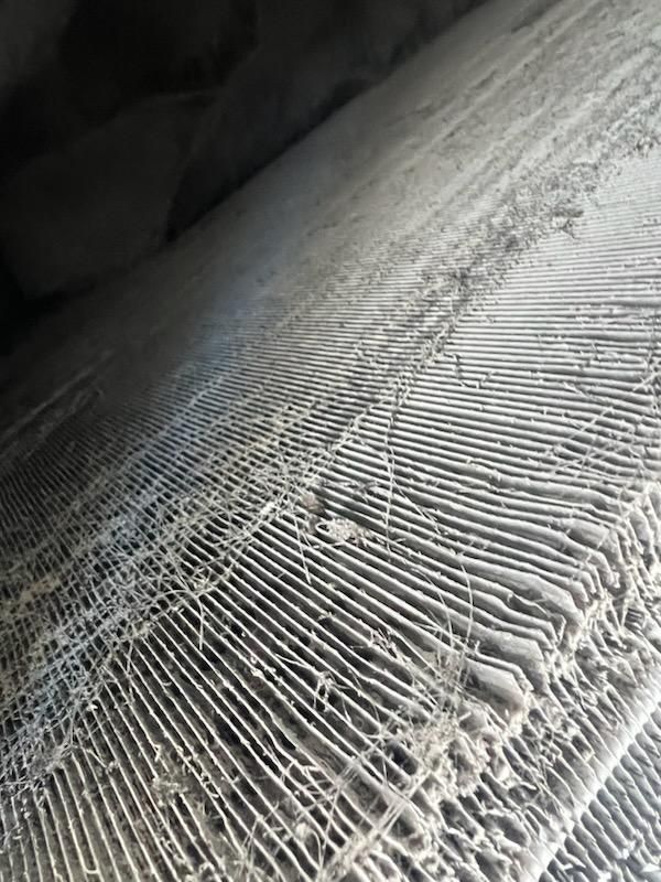 Close-up view of dirty air conditioner fins, covered in dust and debris.