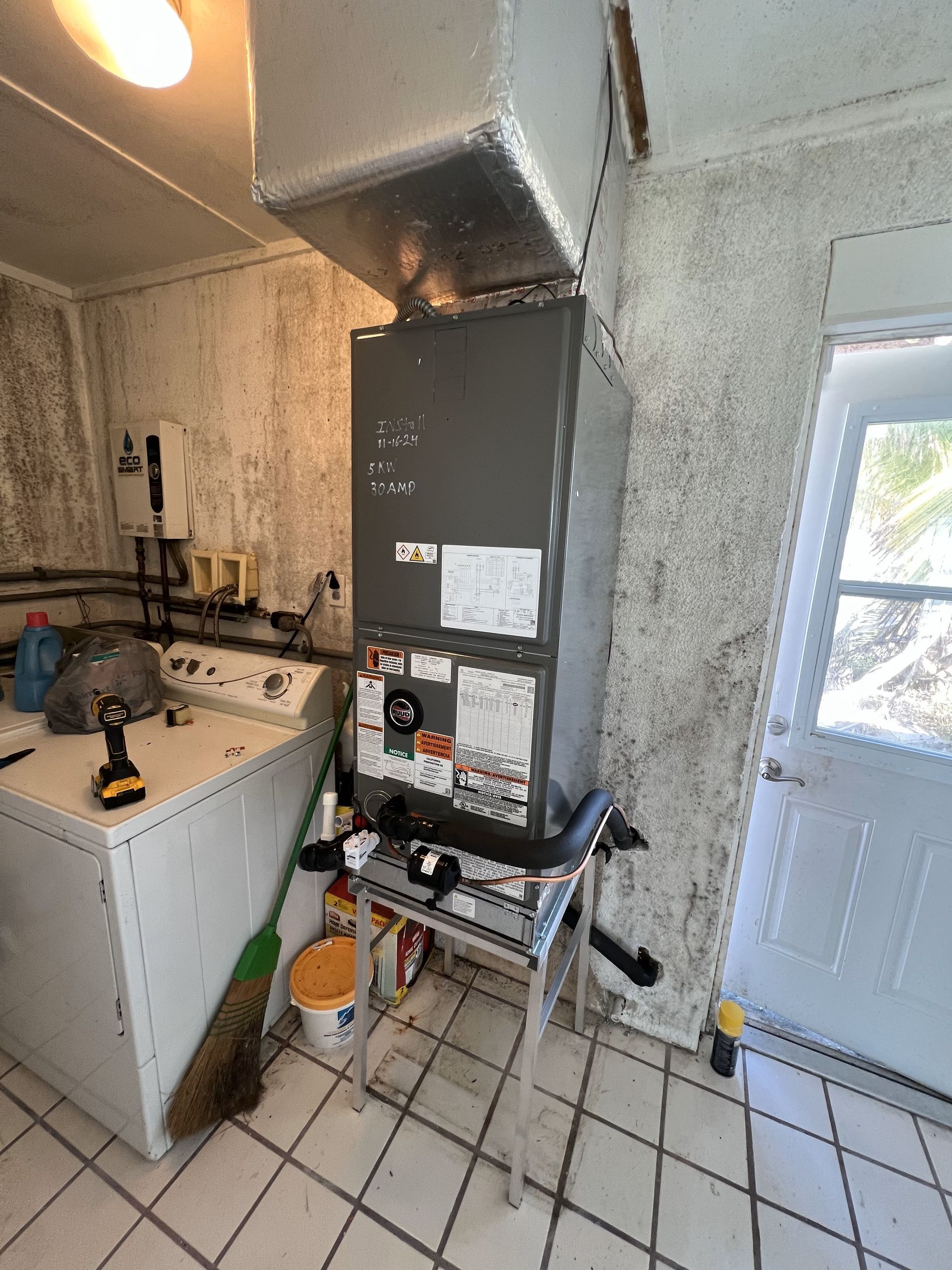 HVAC unit on a stand in a room with a washing machine and moldy walls.