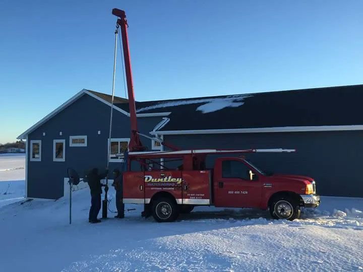 Red tow truck lifting a utility pole beside a blue building in snowy daylight.