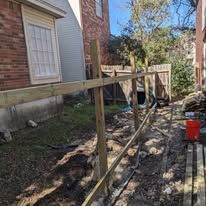 Wooden fence under construction next to a brick building and a yard filled with dirt and construction debris.