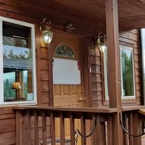 Exterior of a cabin with a wooden porch, windows, and decorative lights.