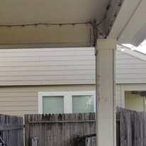 Exterior view of a porch with peeling paint on a support column, overlooking a wooden fence and windows.