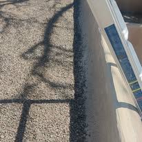 Shadow of a tree on a gravel ground. Light tan wall and a white object in frame.