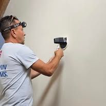Man with headlamp inspects a wall with a device in his hand.