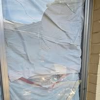 A window covered in tattered white fabric, possibly a sheet, with visible shattered glass.