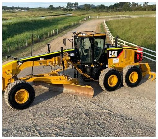 A yellow cat tractor is parked on the side of a dirt road