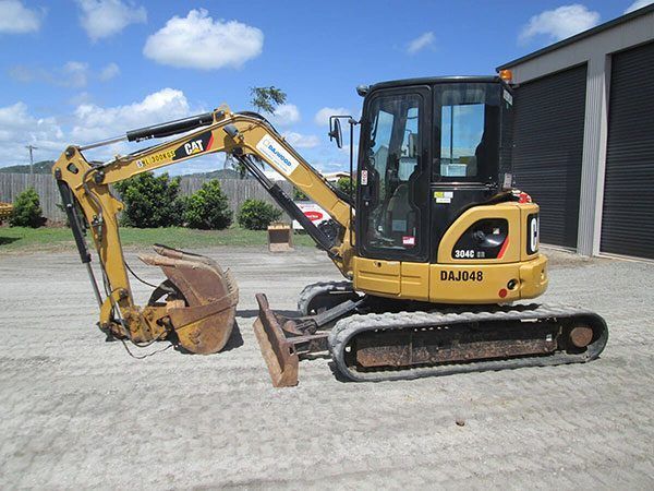 A small yellow excavator is parked in a parking lot.
