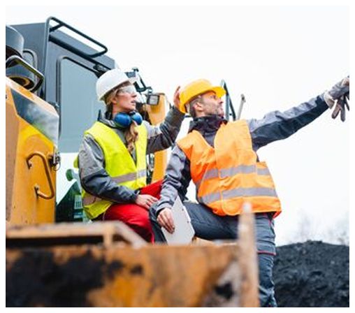 Two construction workers are sitting on a bulldozer at a construction site.