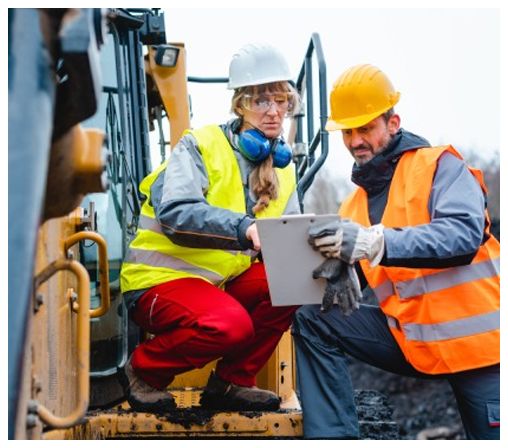A man and a woman are looking at a tablet on a construction site.