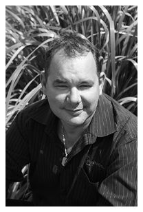 A man in a striped shirt is smiling in a black and white photo.
