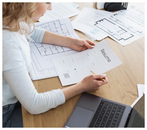 A woman is sitting at a table with a laptop and a resume.