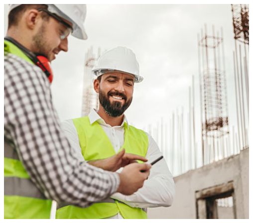 Two construction workers are looking at a cell phone on a construction site.