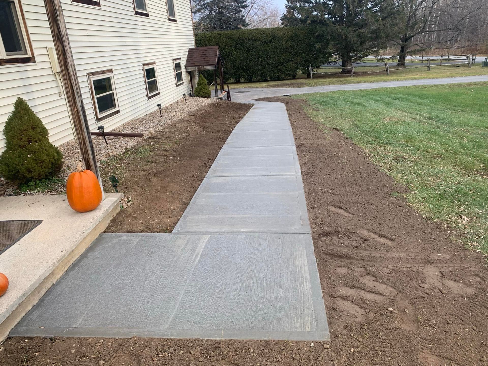 Concrete walkway beside house with fresh soil and a pumpkin on the porch
