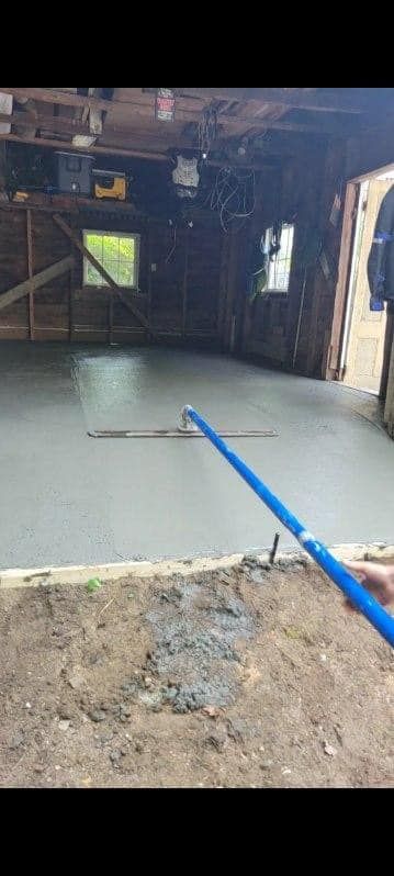 Blue hose spraying water onto a wet concrete floor inside a dark, unfinished room with open doorway.