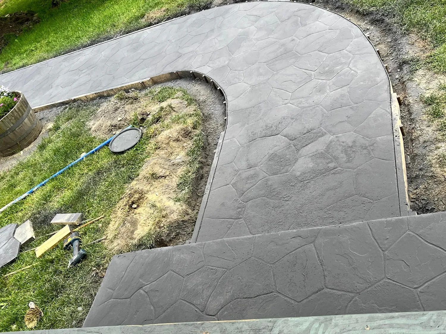 Curving gray concrete walkway bordered by grass and garden tools