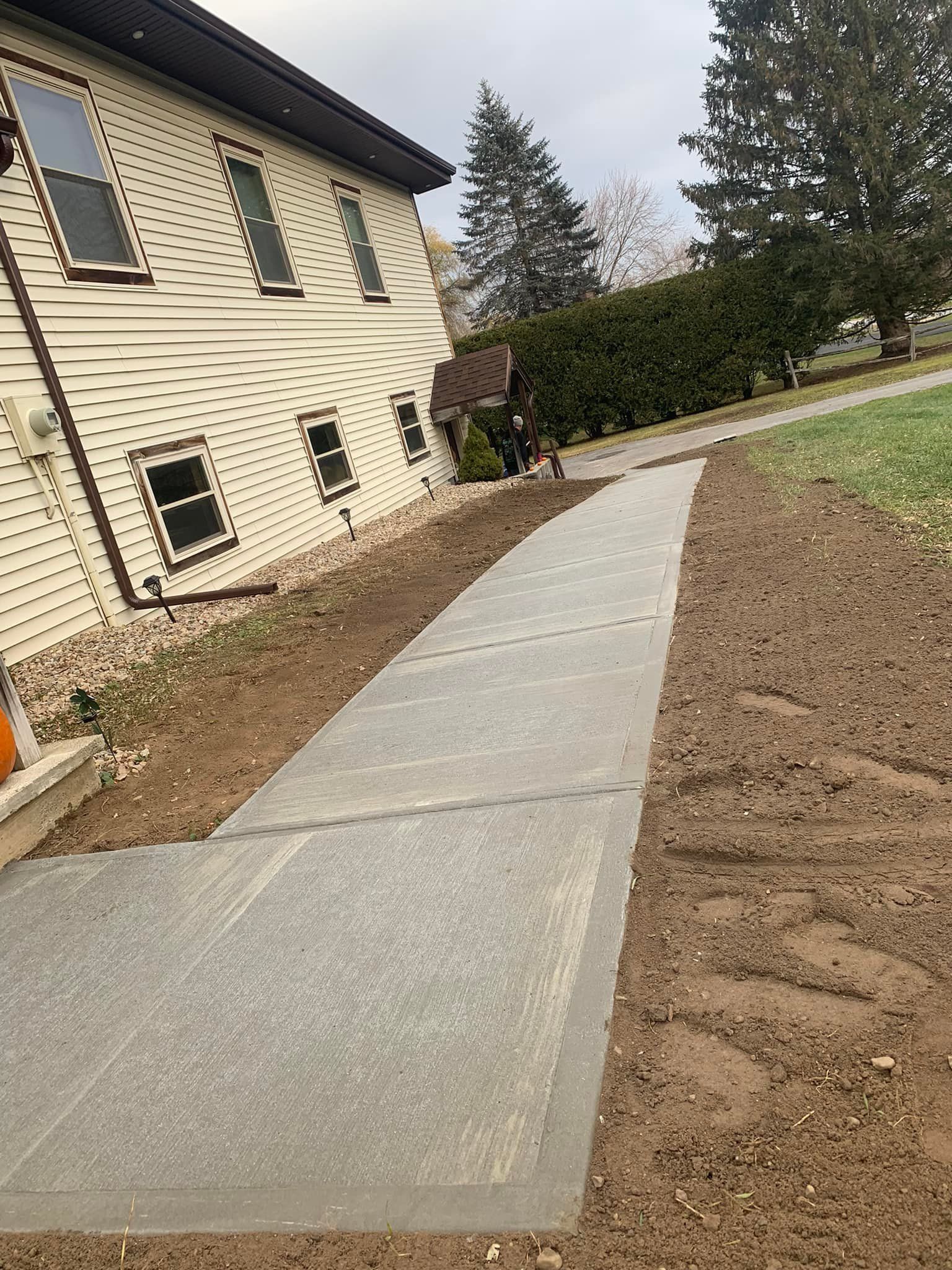 Concrete sidewalk beside a house, curving through a yard under construction.