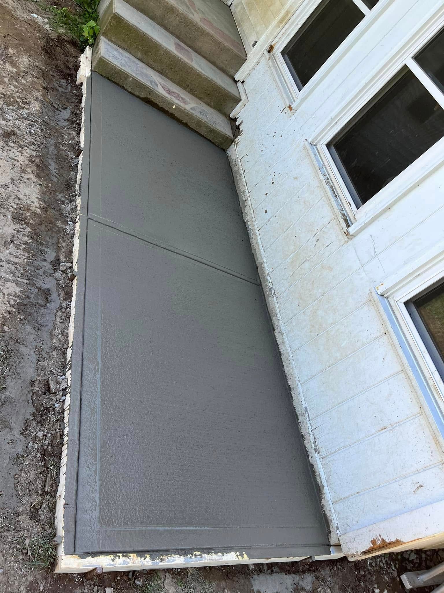 Gray concrete patio beside a white house wall and windows, with steps leading down on the left.