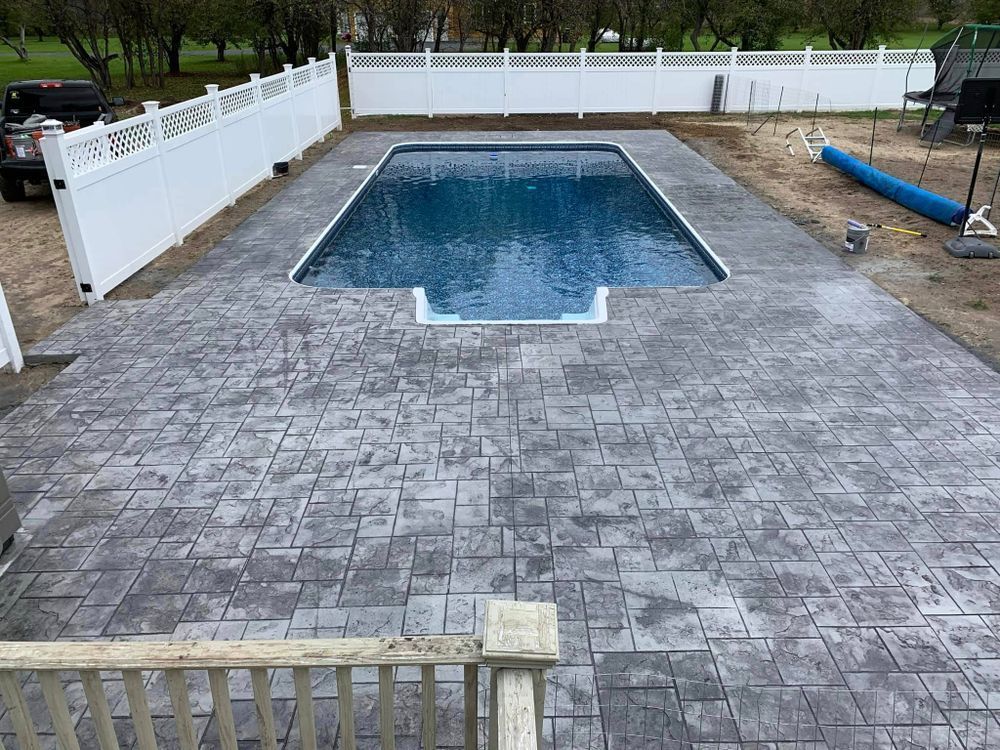 Backyard patio with a fenced in-ground swimming pool and gray stamped concrete deck
