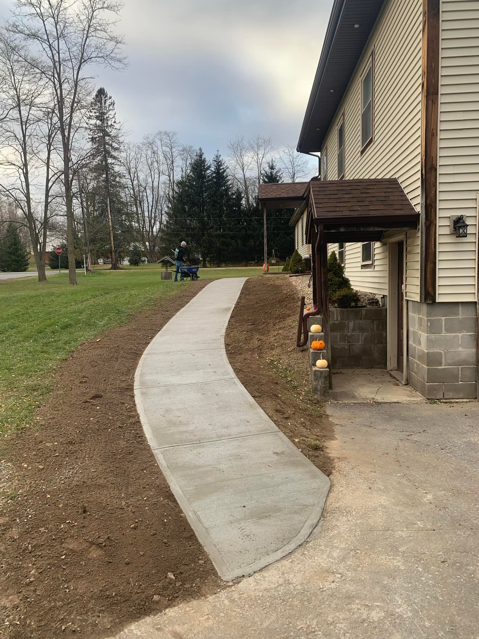 Curved concrete walkway beside a tan house, leading through a grassy yard under a cloudy sky