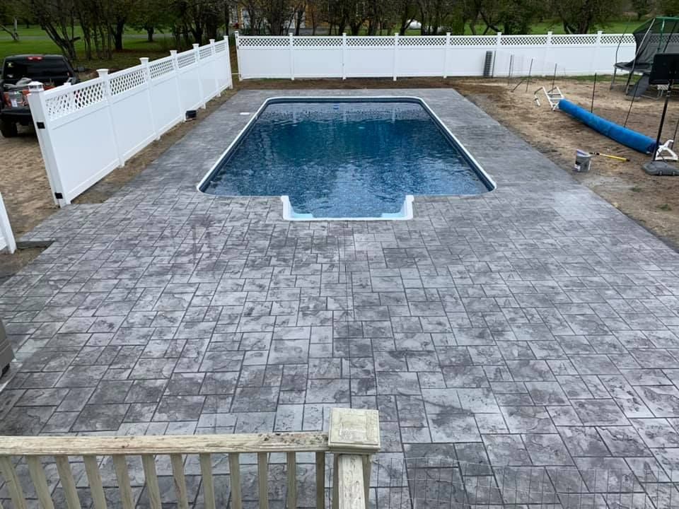 Backyard patio with an empty rectangular in-ground pool surrounded by a stone deck and white fence